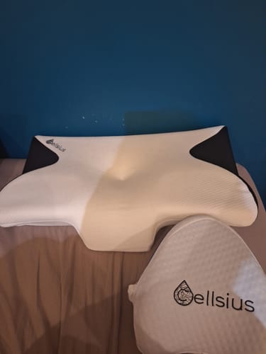 Un client montre le coussin d'alignement cervical Cellsius sur un lit, avec un deuxième article de la marque à côté.