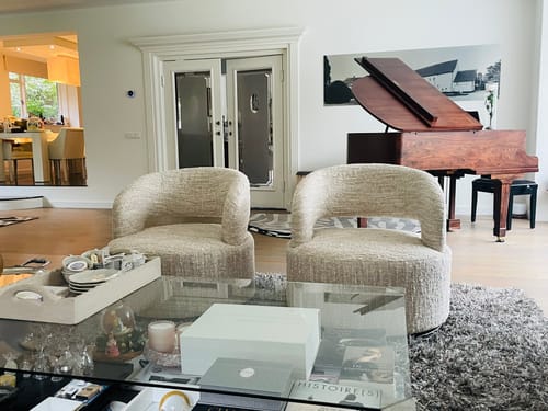 Recensent toont twee beige Kisa draaifauteuils in een ruime woonkamer naast een piano.