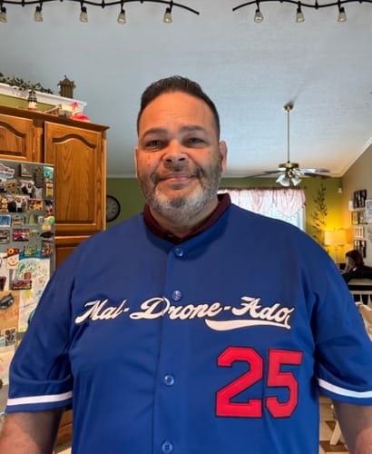 Customer wearing a custom blue baseball jersey with white script across the chest and a red number 25.