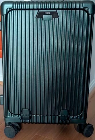 A customer's dark green ribbed All-in-One Carry-On suitcase standing upright on a wooden floor.