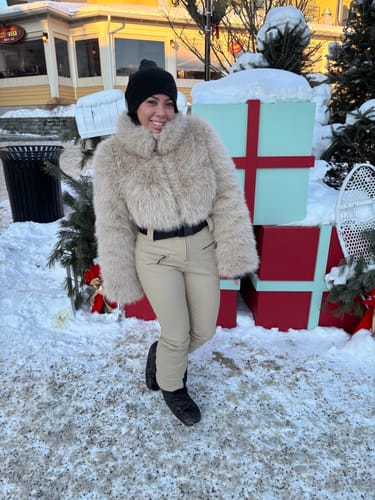 Reviewer smiles in a snowy setting, wearing the khaki slim-fit ski suit with a faux fur jacket.