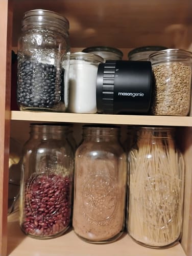 A customer's black Mason Genie vacuum sealer on a pantry shelf next to sealed glass jars of dry goods.