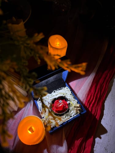 Customer's Gold Mystic Aura Solitaire Diamond Ring in its blue gift box, set in a red rose holder with candles.