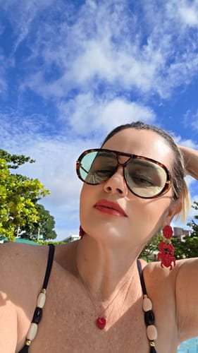 Cliente usando os Óculos Tropea com armação tartaruga e lentes verdes sob um céu azul.