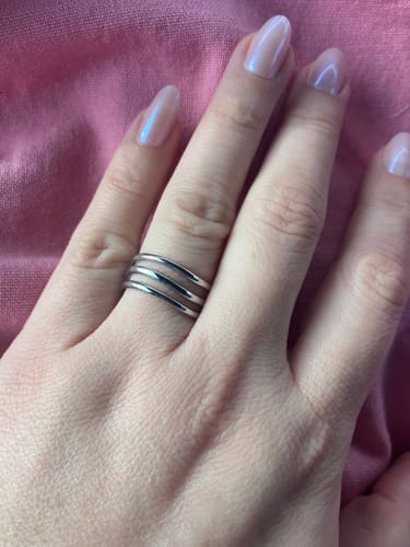 Customer's hand wearing the Kiya Layered Silver Ring on their finger against a pink background.