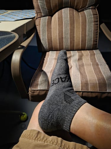 Customer's foot in a grey, ankle-cut alpaca sock, propped up on a striped patio chair.