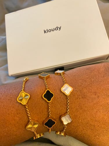 Customer displays three different gold-tone bracelets with clover charms on their arm.