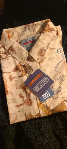 Customer's new 'Book of Dragons' shirt, folded neatly with tags attached, showing the detailed sketch pattern of dragons.