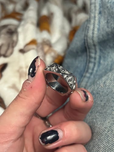 Close-up of a customer's hand holding the chunky, engraved ASTROLOGY RING against a blurred background.
