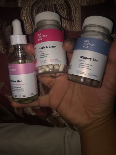 Customer holding the Her Fantasy Bundle products: Renew Her oil, Fresh & Clean suppositories, and Slippery Box capsules.