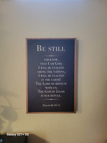 Customer's 'Be Still' faith sign with a dark background and wood frame, hanging on their kitchen wall.