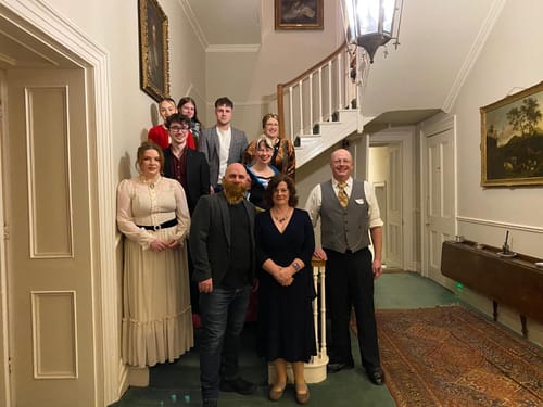 A group of reviewers in period costumes posing on a staircase during their Sherlock Holmes Murder Mystery game night.