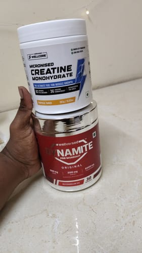 Customer holding a red tub of Dynamite Pre-Workout and a white tub of creatine as mentioned in their review.