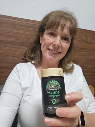 Eine Kundin hält lächelnd eine Flasche der Omega 3 Algenöl Kapseln in die Kamera.