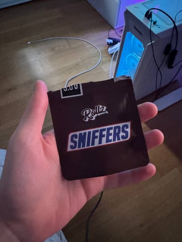 A customer holds the dark brown packaging for Rollz SNIFFERS THCA Flower in their hand.