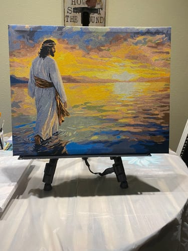 Customer's completed Divine Sunset paint by numbers canvas showing Jesus by the water at sunset, resting on an easel.