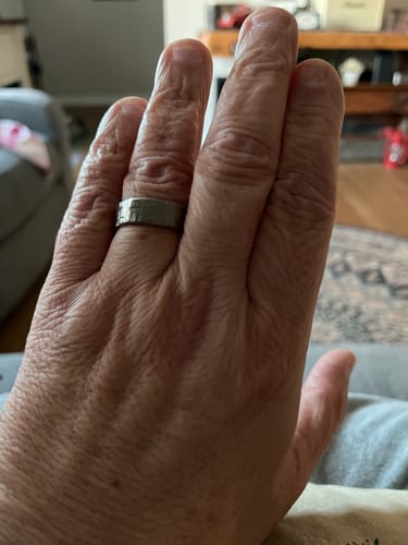 Customer's hand wearing the wide, hammered Terra titanium ring indoors.