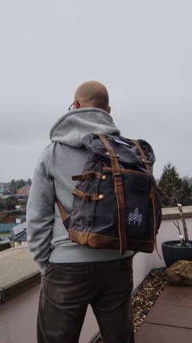 Rückansicht eines Rezensenten, der den grauen Rucksack mit Patch und braunen Lederriemen trägt.