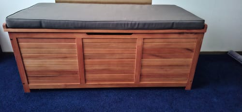 Recensent gebruikt de houten tuinbox met een donkergrijs kussen binnenshuis op een blauw tapijt.