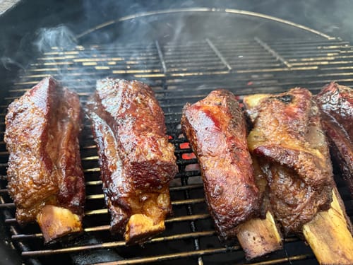 Cliente mostrando unas deliciosas costillas de res ahumándose en una parrilla.