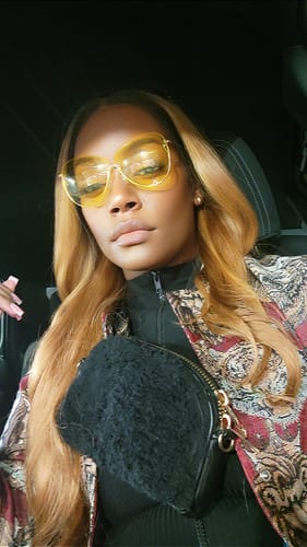 A reviewer wearing the long, blonde Outre Melted Hairline wig with dark roots while sitting in a car.