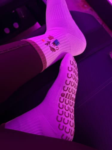 Reviewer showing off their white I'm Just A Girl socks, displaying the grip sole and embroidered ankle graphics.