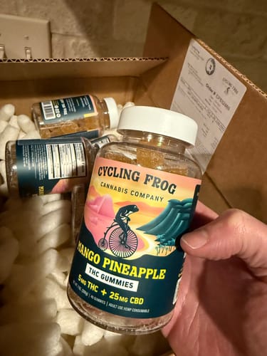 Customer holding a clear jar of Mango-Pineapple Gummies, with more jars visible inside a shipping box.