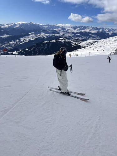 Reviewer standing on a snowy mountain slope wearing the beige baggy waterproof snow pants.