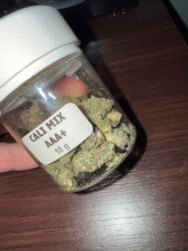 Customer holding a clear 10g jar of CALI MIX AAA+ showing the green buds inside.