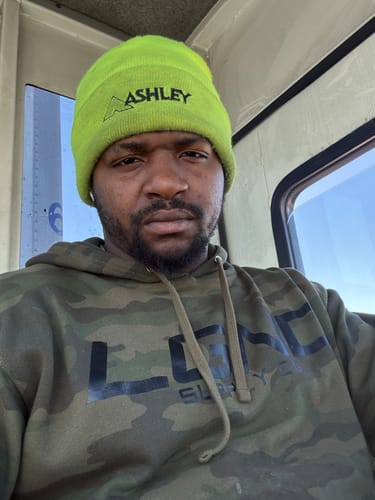 Customer wearing a camouflage hoodie and a bright green beanie, taking a selfie inside a cabin.