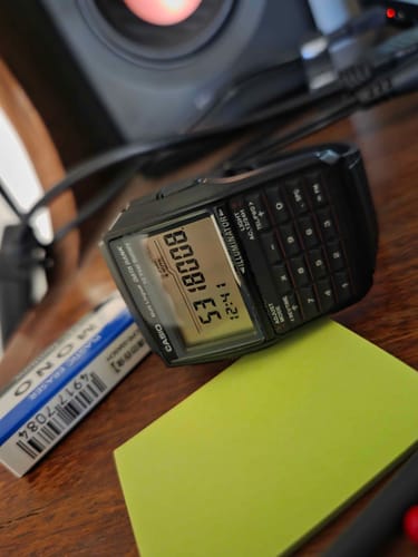 El reloj calculadora Casio Databank de un cliente sobre un escritorio de madera con la pantalla encendida.