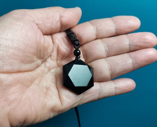 Un client tenant le collier d'obsidienne avec son pendentif hexagonal noir dans la main.