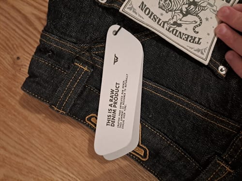 Customer's close-up of the new Raw Baggy Denim Jeans, showing the white product tag and durable yellow stitching.