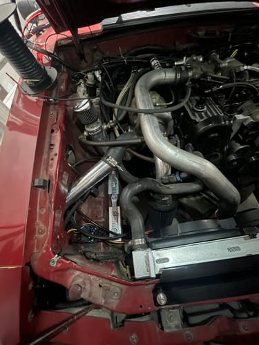 Customer's Billet IGN1A Coil Mount installed vertically in the front driver's side of a red car's engine bay.