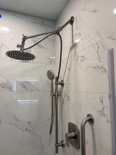 Customer's brushed nickel Adjustable Shower Arm installed in a tiled shower, holding a rain shower head.
