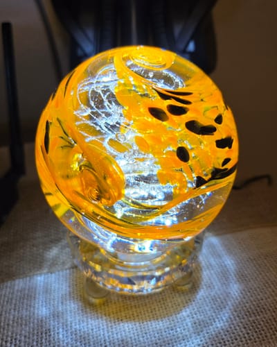 Customer's glowing Motorcycle Memorial orb on a lighted stand. The orange and black glass contains infused ash.