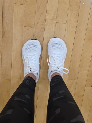 Reviewer's perspective looking down at their white MUUV Flow pickleball shoes on a wooden floor.