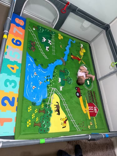 A customer's baby lying on a colorful, padded play mat inside a playpen.