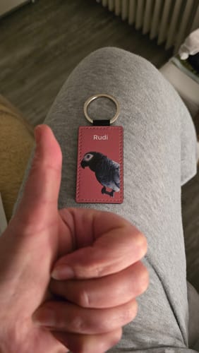 Kunde zeigt Daumen hoch für einen rosa Schlüsselanhänger mit einem Haustierportrait eines Papageis namens 'Rudi'.