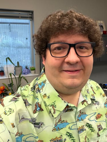 A reviewer smiles while wearing the light green Jurassic Park "Park Map" short sleeve shirt.