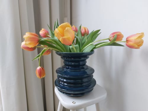 Recensent toont de donkergroene POLSPOTTEN Stacked Plates Vaas gevuld met kleurrijke tulpen.