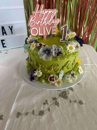Customer's green birthday cake decorated with colorful freeze-dried edible pansies for a first birthday.
