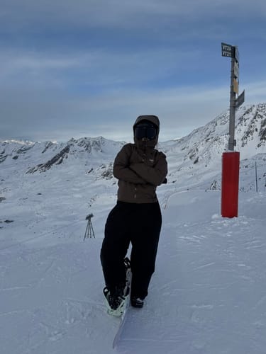 Reviewer wearing the black baggy snow pants while standing with a snowboard on a snowy mountain.