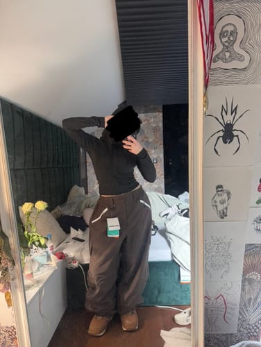 Reviewer in a mirror wearing the new baggy snow pants with the tag still attached.