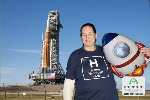 Reviewer smiling in a dark blue Blame Hydrogen T-shirt, standing in front of a rocket.