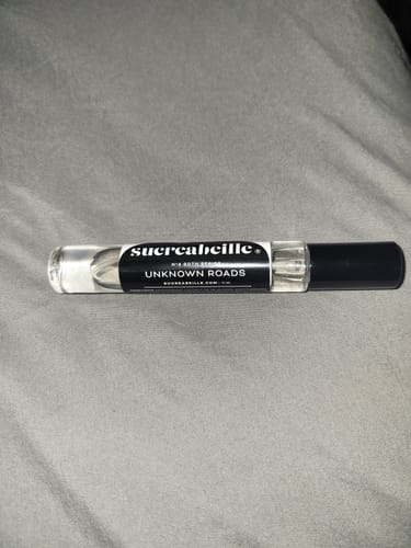 Reviewer's Unknown Roads rollerball perfume bottle lying on a grey textured fabric.