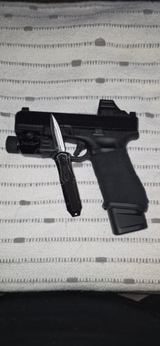 Reviewer's black VT Mini Missile OTF knife with its blade extended, placed on a handgun to show its compact size for EDC.