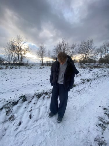 Customer wearing the Black Puffer Jacket over a hoodie while standing in a snowy field.