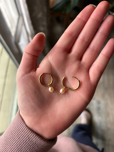 Customer holding a pair of gold Bella Hoop Earrings with subtle pink pearls in their palm.