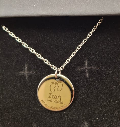 Customer's silver-colored Newborn necklace with a round pendant engraved with baby's birth details, resting in a black box.